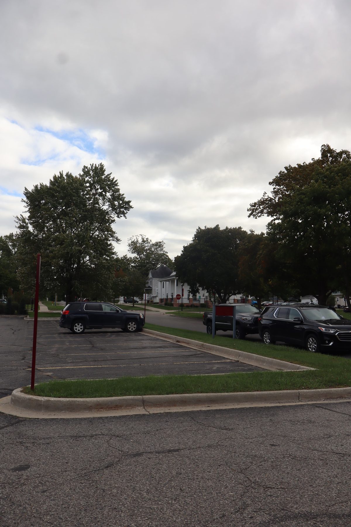 A car park with a few cars, a white house across the road